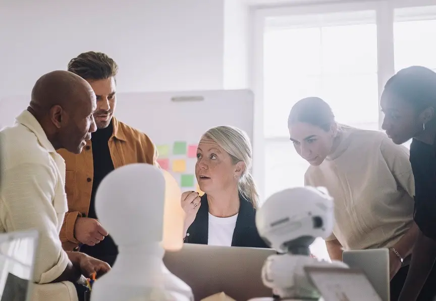 En grupp personer runt ett bord som diskutera och arbetar med en AI-robot